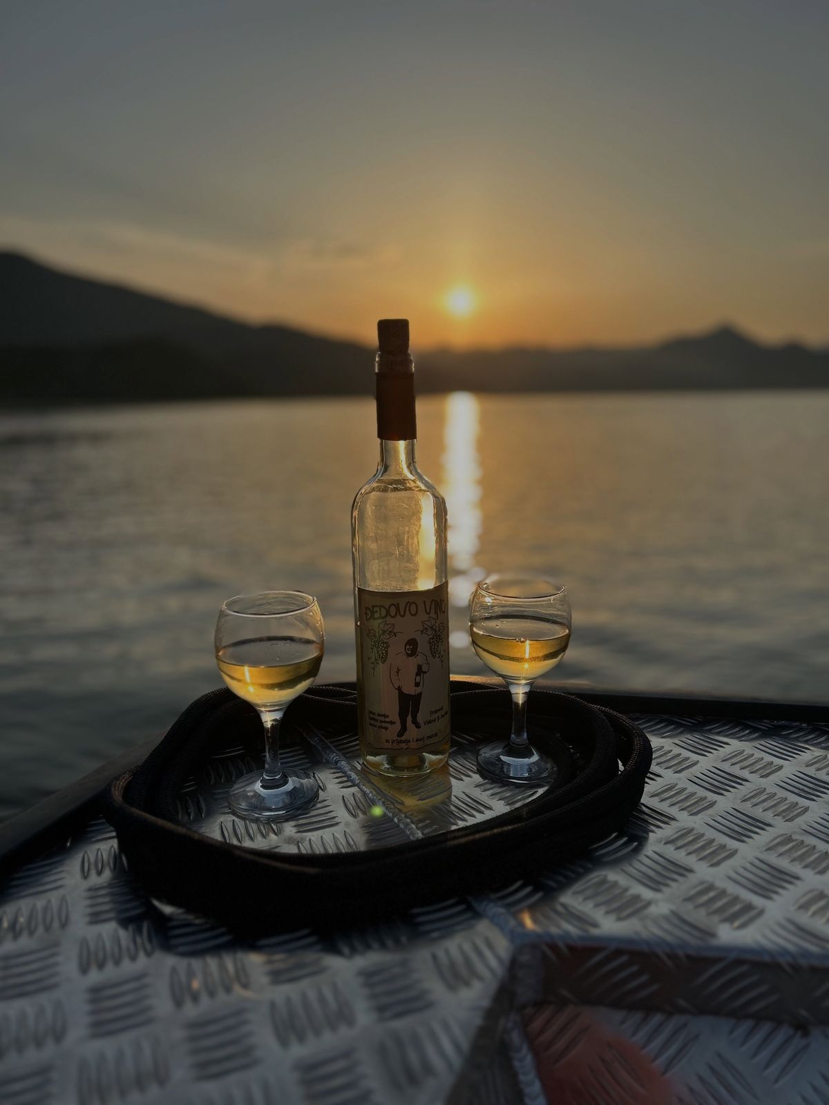 Zalazak sunca nad jezerom, boca vina i dvije čaše na brodu